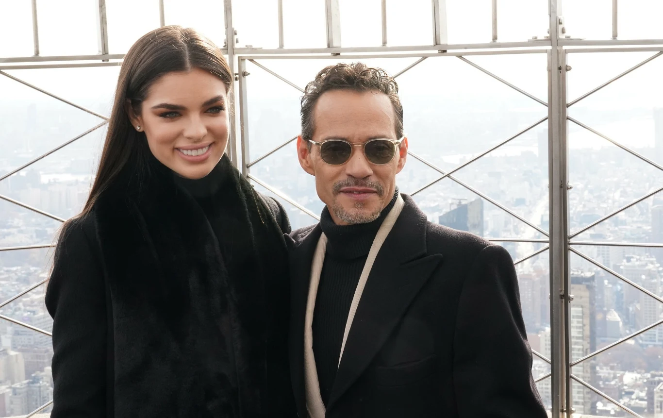 Para elegancko ubranych osób pozuje do zdjęcia na tle metalowej konstrukcji z panoramicznym widokiem na nowoczesne miasto w tle.