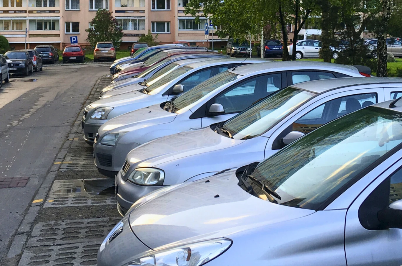 3 zł za godz. albo 150 zł miesięcznie. Koniec darmowego parkingu pod blokiem. Szereg zaparkowanych samochodów na parkingu osiedlowym przy blokach mieszkalnych, widoczna zieleń oraz kilka drzew w tle.