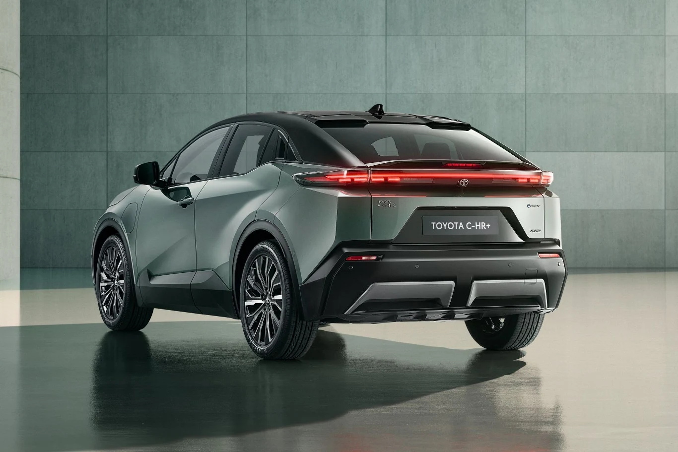 Nowoczesny samochód Toyota C-HR w odcieniu szarości, sfotografowany z tyłu w jasnym, minimalistycznym otoczeniu. Smukłe linie nadwozia, chromowane detale oraz charakterystyczny pasek świateł LED na tylnej klapie podkreślają sportowy charakter pojazdu.