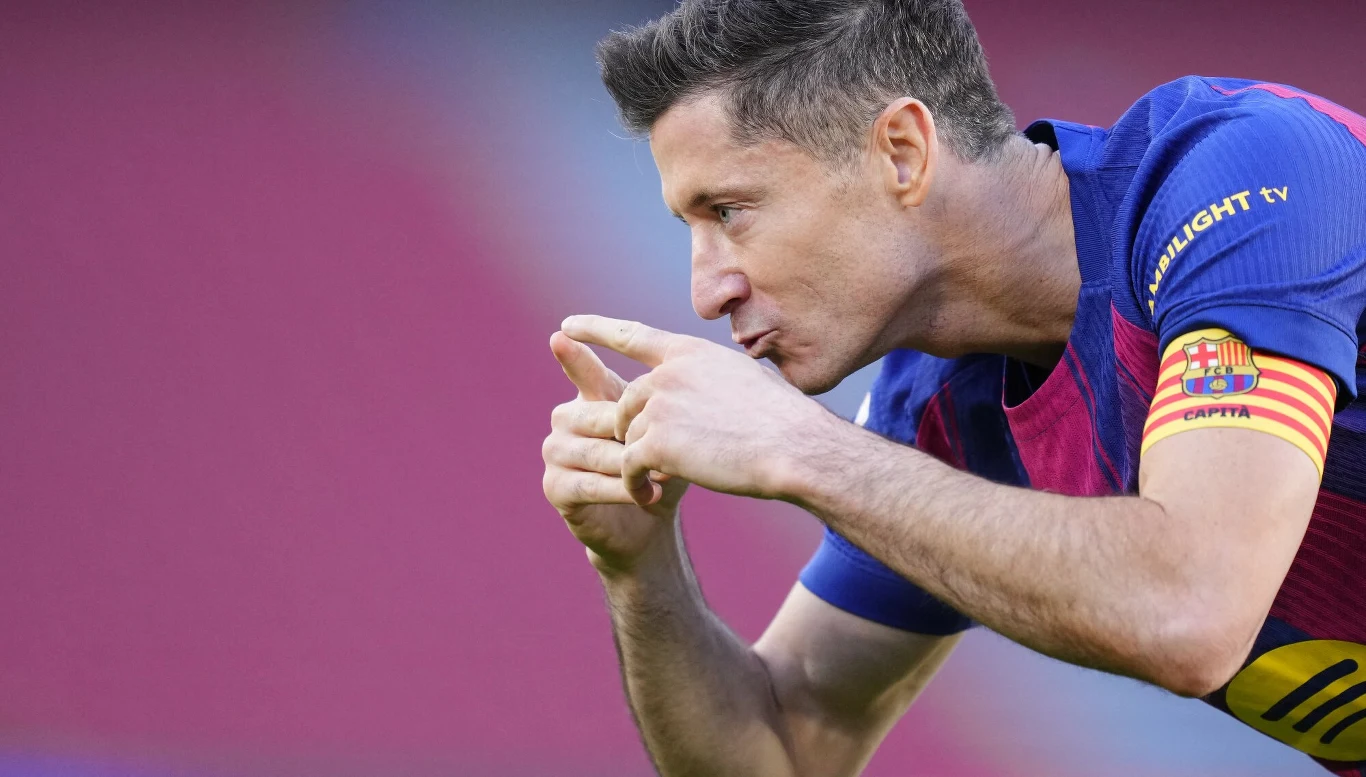 Robert Lewandowski Piłkarz w koszulce FC Barcelony wykonuje gest rękami podczas meczu, na ramieniu opaska kapitańska w kolorach żółto-czerwonych.