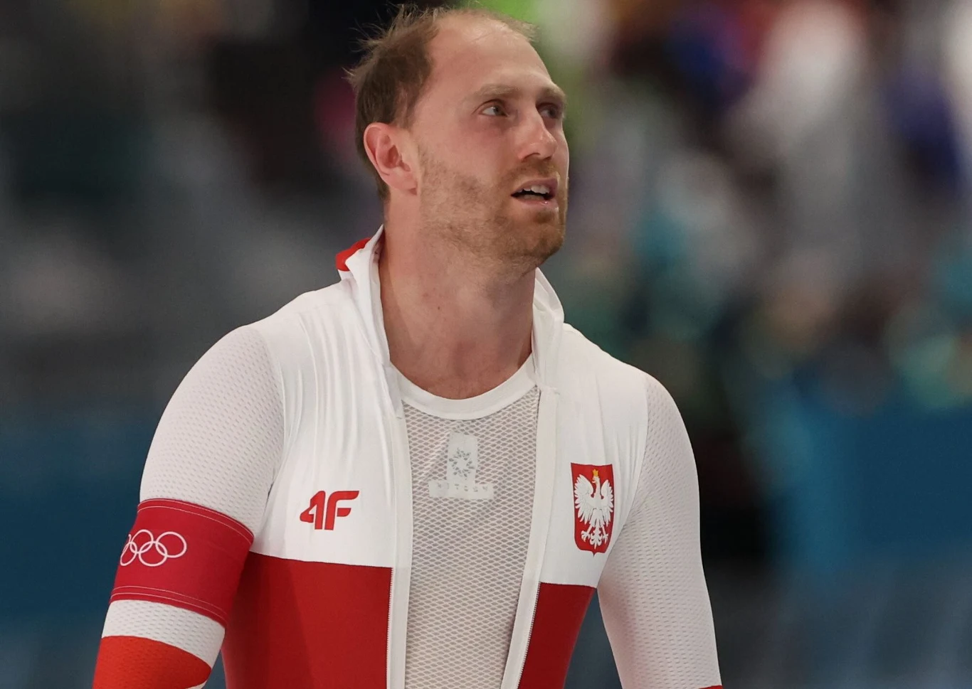 Damian Żurek Sportowiec w biało-czerwonym stroju z godłem Polski oraz logo olimpijskim na rękawie, widoczny z wyrazem skupienia na twarzy, tło rozmyte, co podkreśla jego sylwetkę i główny motyw zdjęcia.