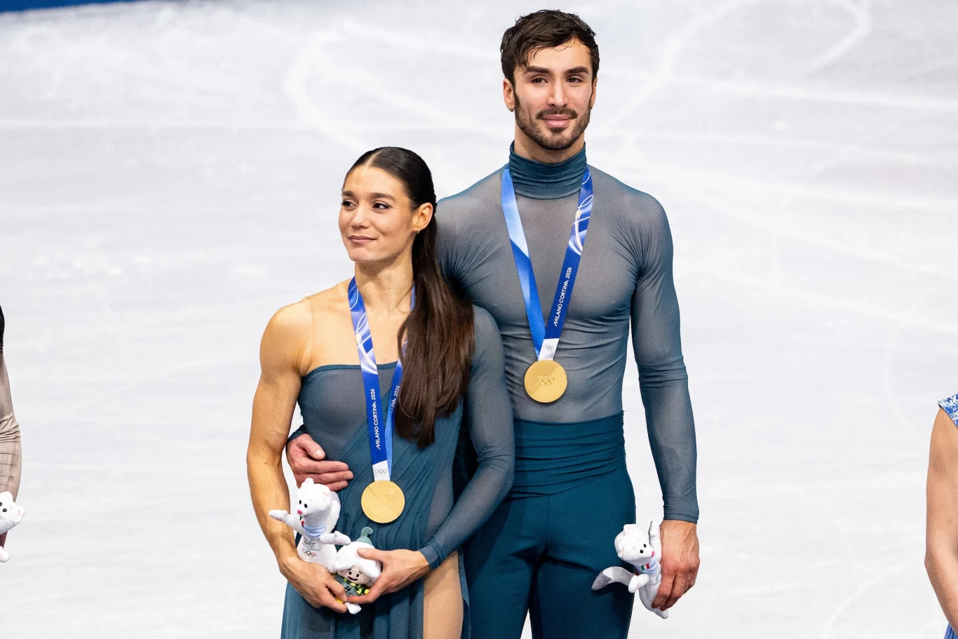 Laurence Fournier Beaudry i Guillaume Cizeron Para łyżwiarzy figurowych na lodowisku, oboje ubrani w stroje sportowe i z medalami złotymi na szyjach, trzymają maskotki, stojąc obok siebie z uśmiechem na twarzach.