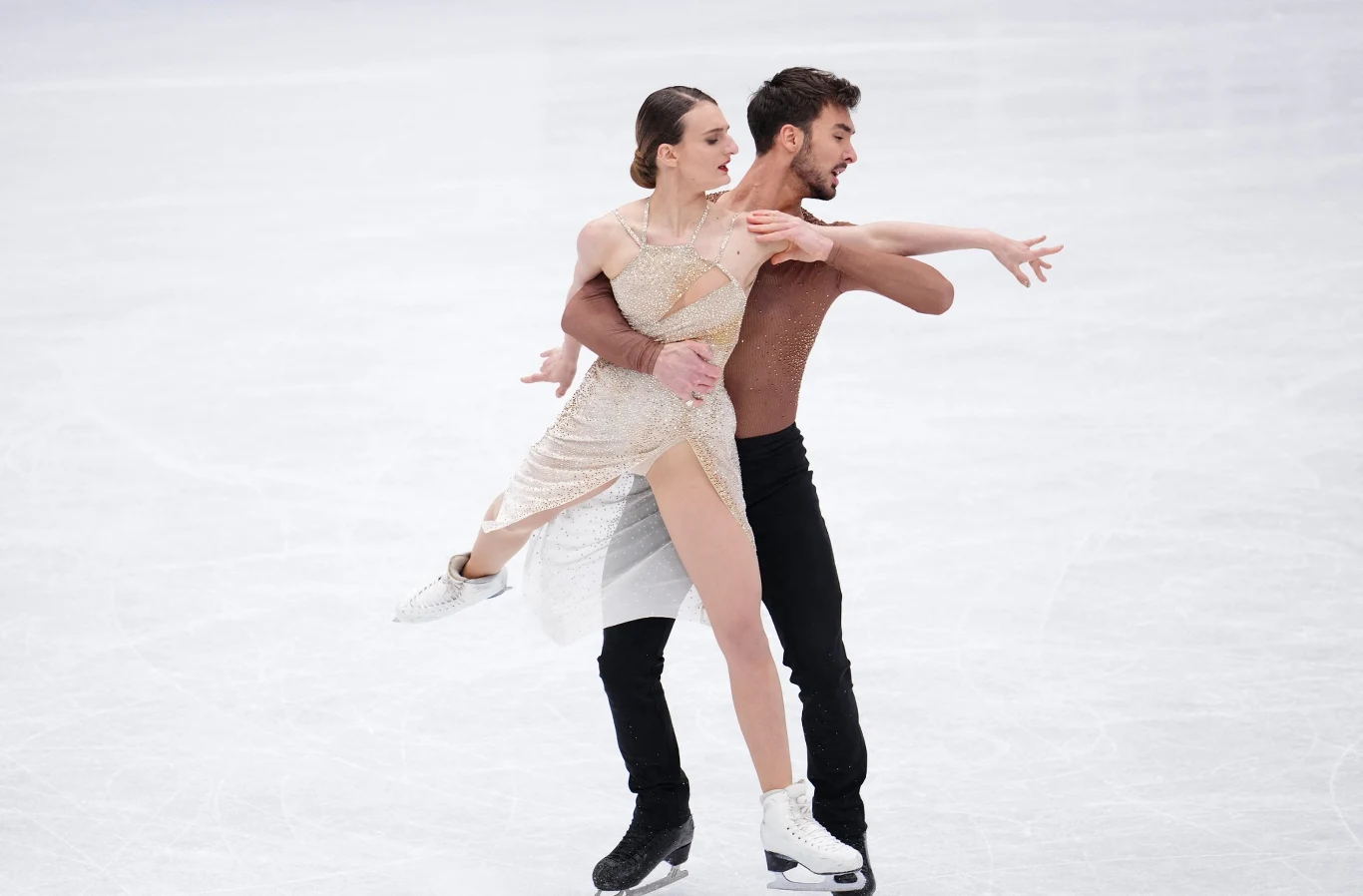 Gabriella Papadakis i Guillaume Cizeron Para łyżwiarzy figurowych podczas występu na lodowisku, kobieta w eleganckiej, jasnej sukni i mężczyzna w ciemnym stroju wykonują zaawansowaną figurę taneczną, oboje skoncentrowani na płynnym ruchu i synchronizacji.