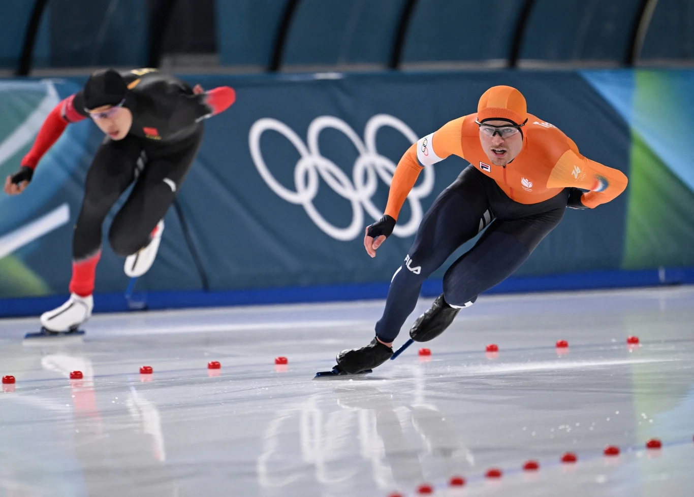 Holender Joep Wennemars po zajechaniu drogi przez Chińczyka stracił szansę na medal olimpijski Dwóch łyżwiarzy szybkich ścigających się na lodowisku podczas zawodów olimpijskich, zawodnik w pomarańczowym stroju jest na prowadzeniu, w tle widoczne logo igrzysk olimpijskich.