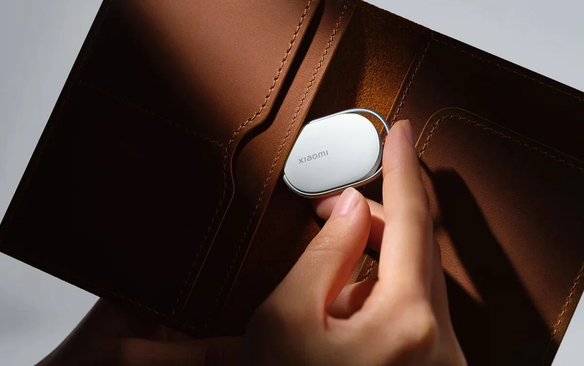 Xiaomi Tag z dobrą ceną. Nowy lokalizator powalczy z AirTag 2. Ręka wkłada miniaturowy lokalizator marki Xiaomi do wnętrza brązowego portfela, w świetle eksponującym gładką fakturę skóry oraz elegancki wygląd urządzenia.