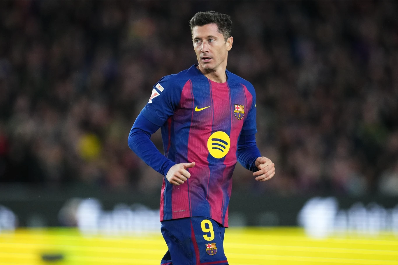 Piłkarz w stroju FC Barcelony na boisku podczas meczu, w tle rozmazani kibice na trybunach.