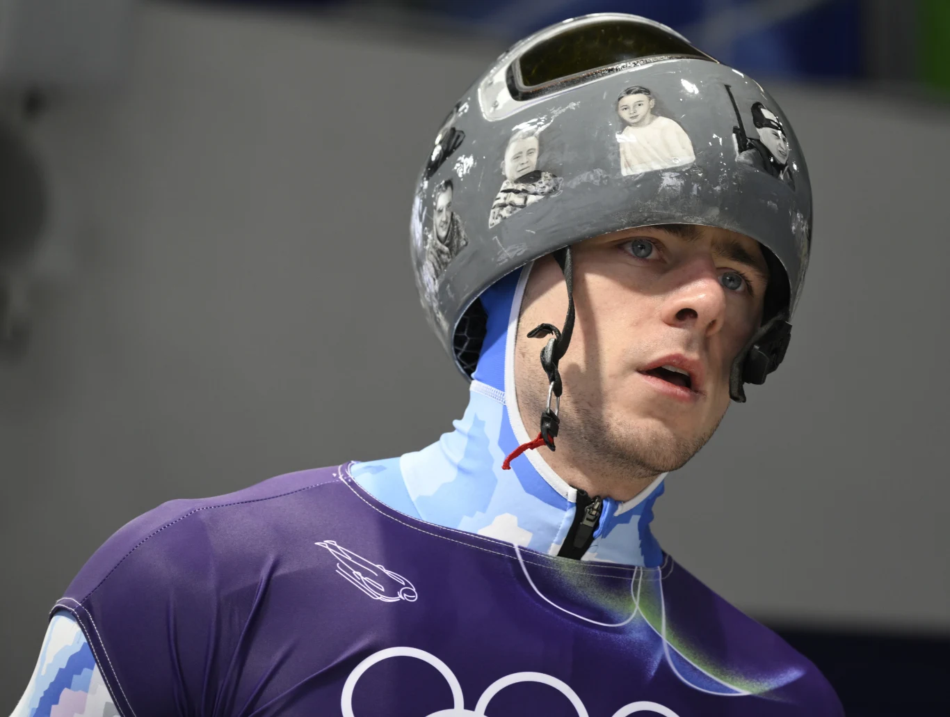 Władysław Heraskewycz Sportowiec w stroju startowym, z kaskiem ozdobionym czarno-białymi ilustracjami i grafiką, skupiony przed startem na zawodach, na tle niewyraźnego stadionu.