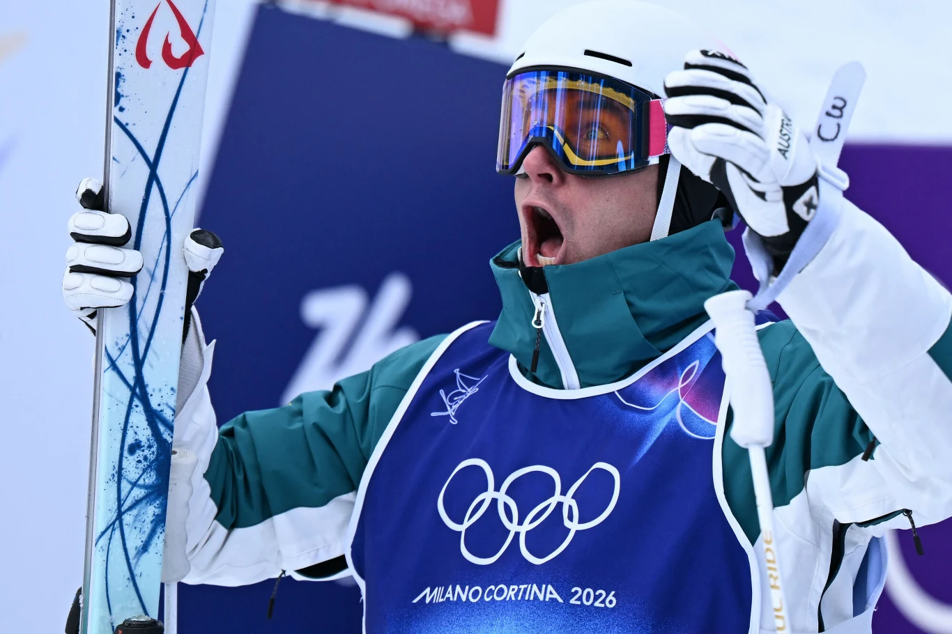 Cooper Woods celebrujący mistrzostwo olimpijskie, 12.02.2026 r. Zawodnik w stroju narciarskim i goglach trzyma narty, wyraża silne emocje, prawdopodobnie radość z wyniku sportowego, na piersi widnieje logo igrzysk olimpijskich Mediolan-Cortina 2026.