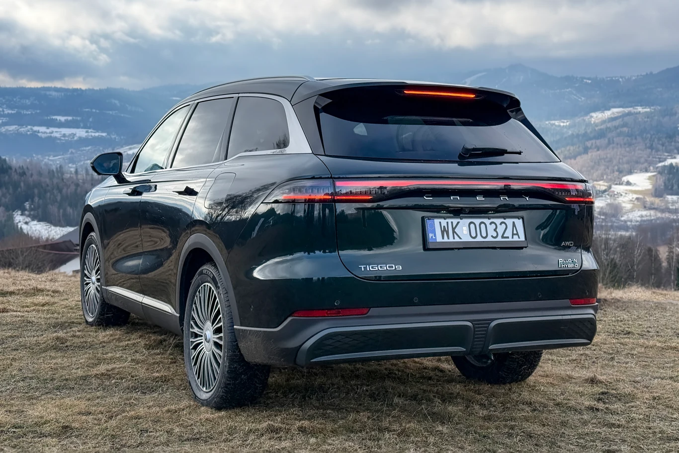 Czarny nowoczesny SUV marki Seres stoi zaparkowany na wzgórzu z widokiem na górski krajobraz, w tle rozciąga się panorama zaśnieżonych pagórków i chmur.