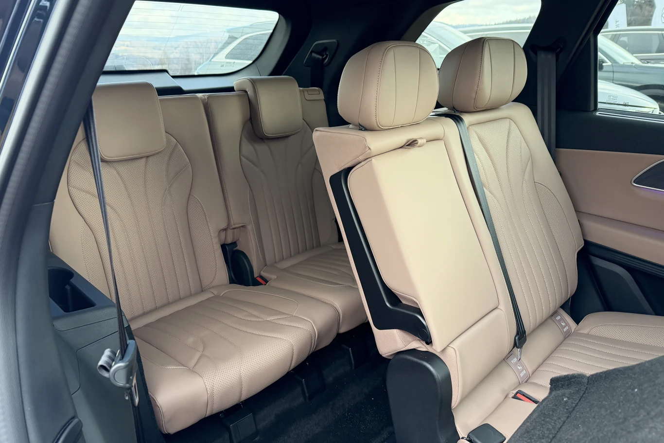 Wnętrze samochodu z rozłożonymi, beżowymi siedzeniami w trzecim rzędzie oraz przesuniętym do przodu jednym z siedzeń drugiego rzędu, umożliwiającym dostęp do tylnej części pojazdu.