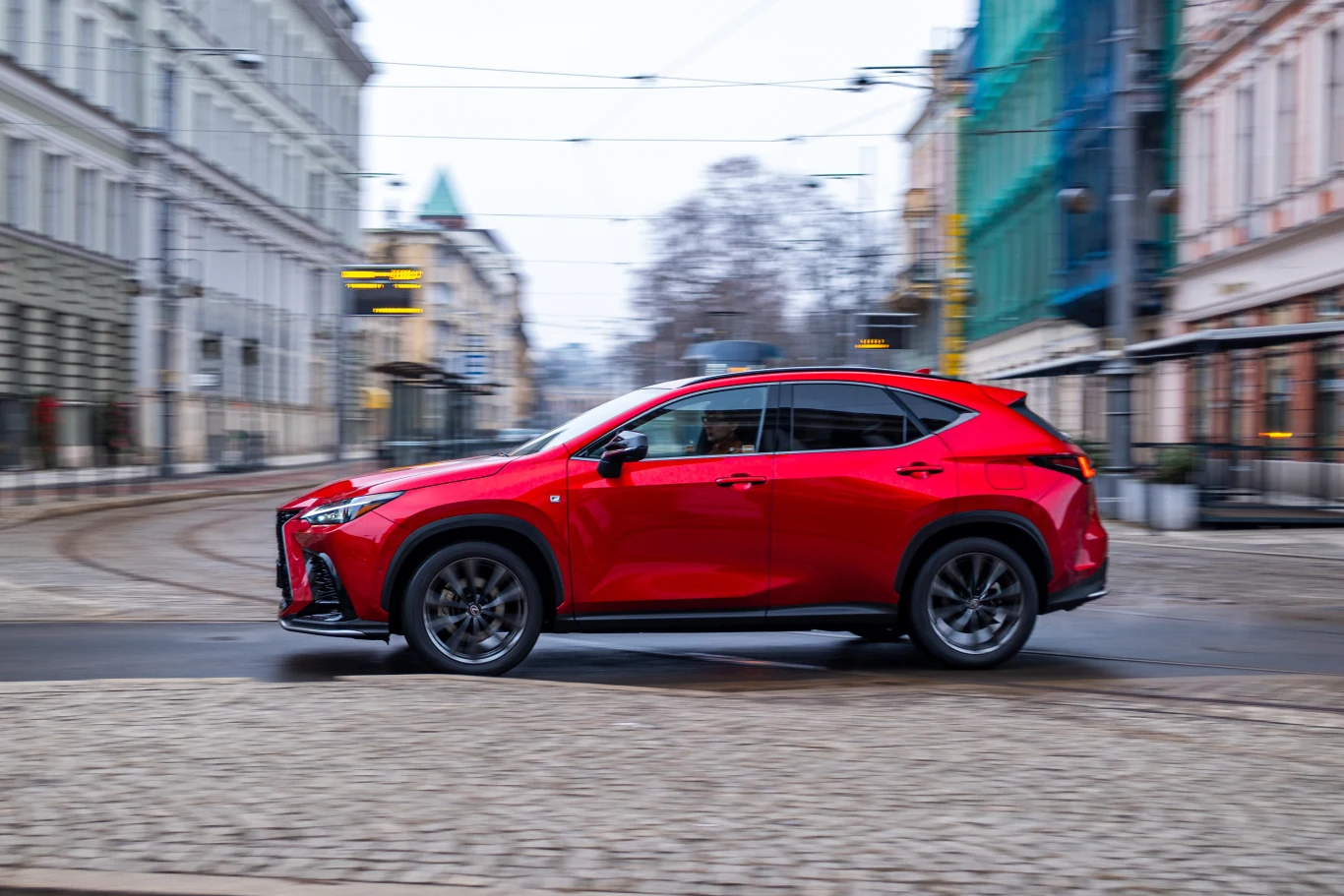 Czerwony samochód typu SUV przejeżdżający przez pustą ulicę miasta z zabytkowymi kamienicami w tle.