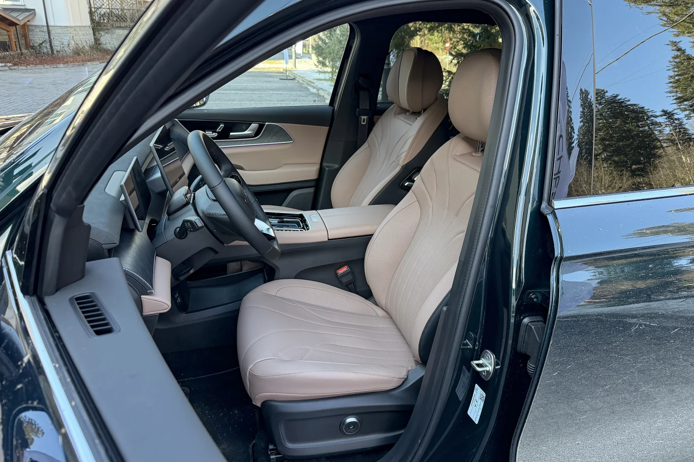 Wnętrze nowoczesnego samochodu z jasnobeżowymi skórzanymi fotelami, kierownicą oraz pulpitem sterującym, drzwi przednie otwarte, widoczne detale deski rozdzielczej i konsoli środkowej.