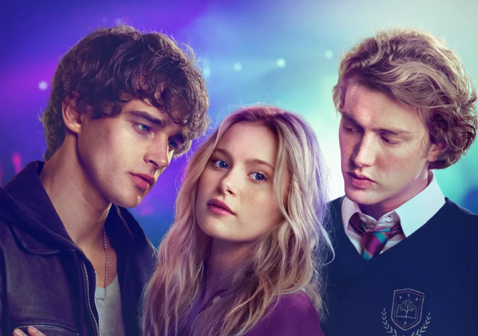 "Love Me, Love Me" Trójka młodych ludzi stoi blisko siebie na tle kolorowych, rozmytych świateł, ich wyraz twarzy sugeruje napięcie emocjonalne lub skomplikowaną relację.