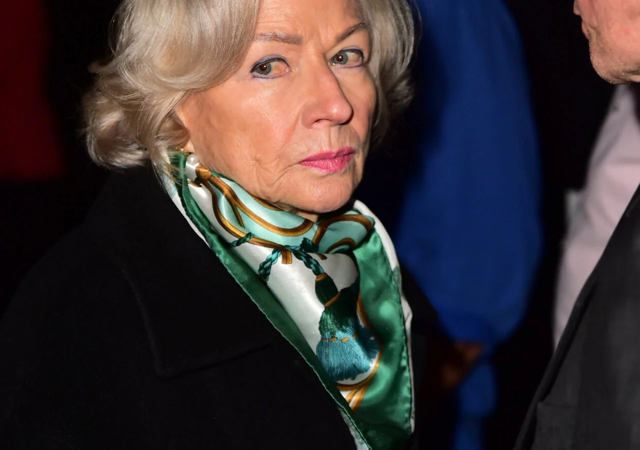 Bożena Dykiel Starsza kobieta o siwych włosach w eleganckim zielonym szaliku z wzorem, ubrana w ciemny płaszcz. Patrzy stanowczo w stronę obiektywu, obok niej widoczna sylwetka innej osoby.