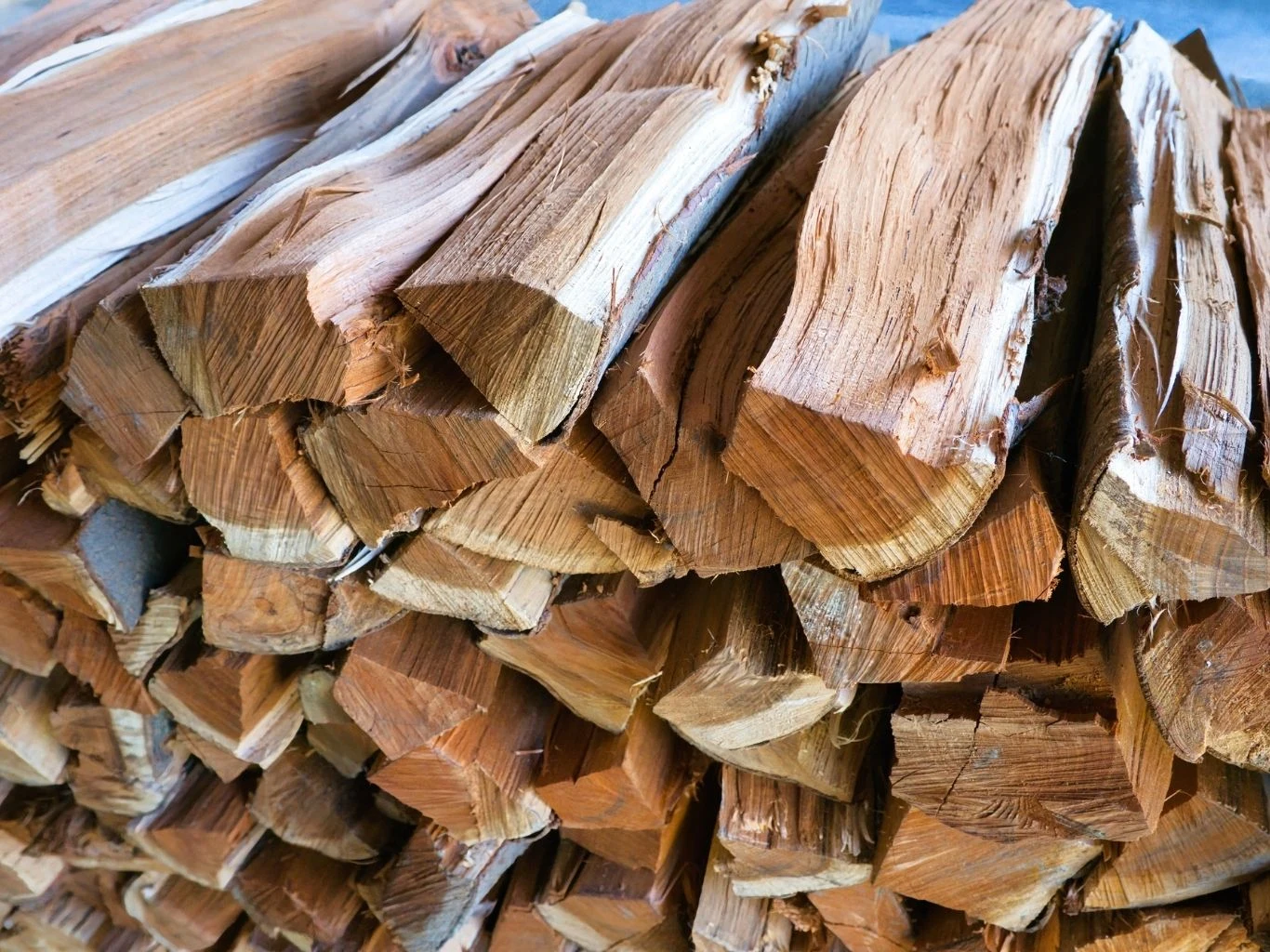 Stos równo ułożonych kawałków drewna opałowego o wyraźnej strukturze słojów i jasnej barwie drewna.