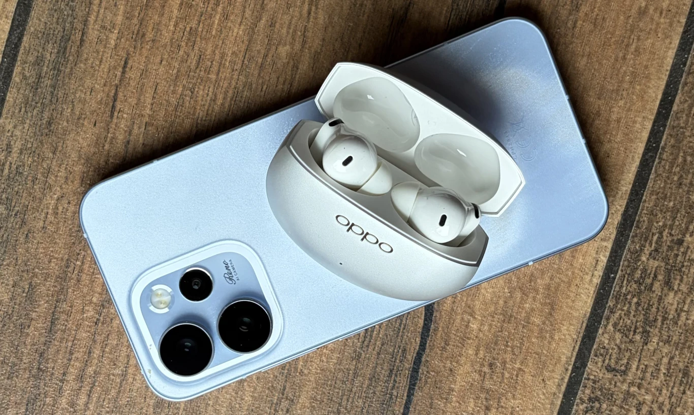 Test OPPO Enco X3s. Sprawdzamy nowe słuchawki bezprzewodowe z ANC. Białe, bezprzewodowe słuchawki Oppo w etui ładującym leżące na srebrnym smartfonie z trzema aparatami i lampą błyskową, całość umieszczona na drewnianej powierzchni.