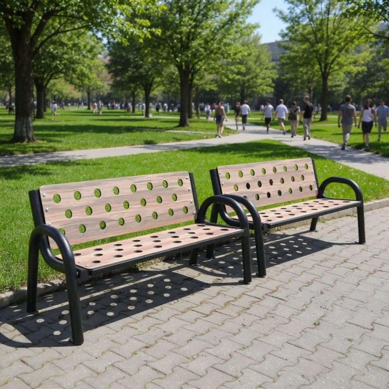 Dwie nowoczesne ławki o metalowej konstrukcji i drewnianych deskach z otworami ustawione na chodniku w zielonym parku, w tle alejki z drzewami oraz spacerujący ludzie.
