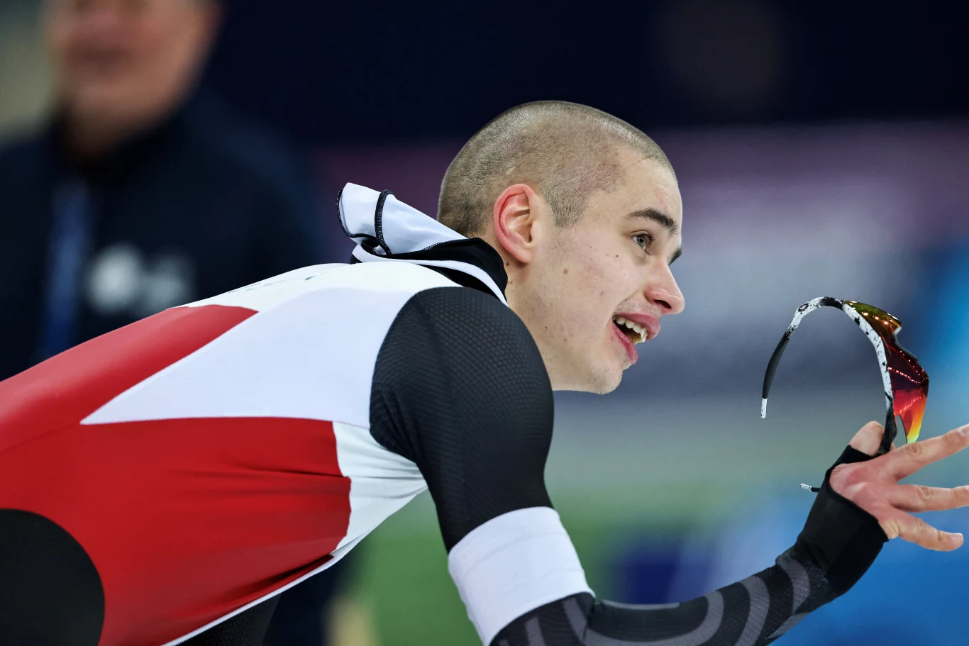 Władimir Semirunnij Łyżwiarz szybki w stroju sportowym pochylony do przodu, trzymający okulary ochronne w dłoni, wyrażający radość lub ulgę po zakończonym wyścigu. W tle rozmazana sylwetka innej osoby.