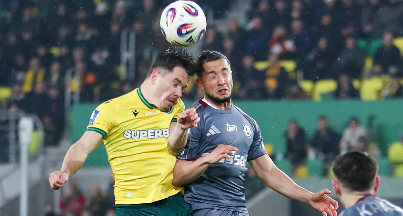 Wahan Biczachczjan (z prawej) dał Legii prowadzenie, ale potem do głosu doszli gospodarze Dwóch piłkarzy walczy o piłkę głową podczas meczu na stadionie, w tle rozmyta publiczność i trybuny.