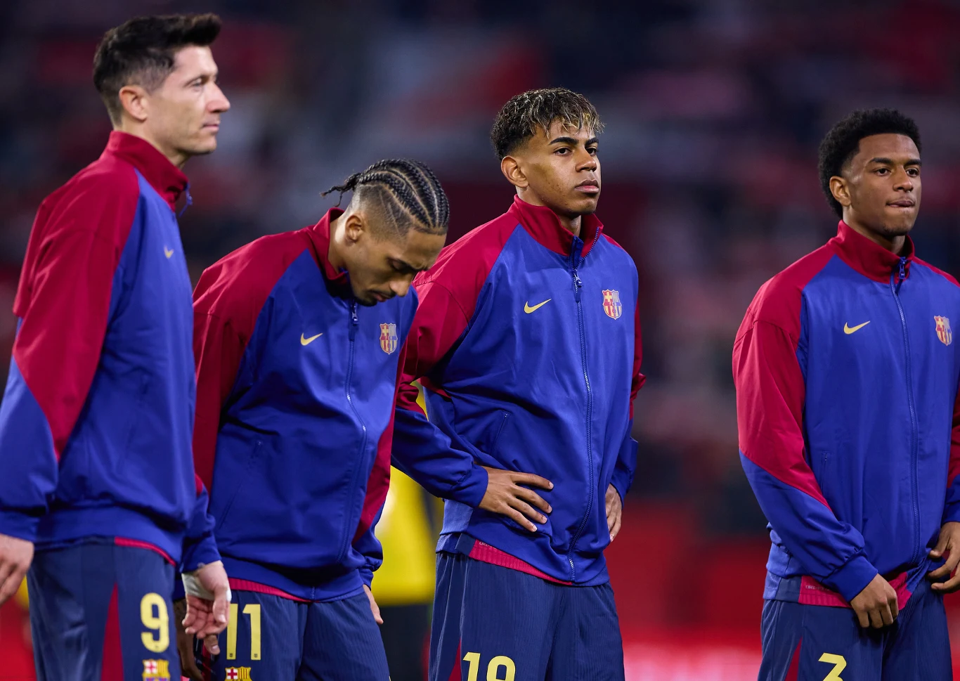 Robert Lewandowski, Raphinha, Lamine Yamal oraz Alejandro Balde Czterech piłkarzy drużyny FC Barcelona w oficjalnych klubowych strojach stoi na murawie stadionu, skupieni na przygotowaniach do meczu, z wyraźnym napięciem i koncentracją na twarzach.