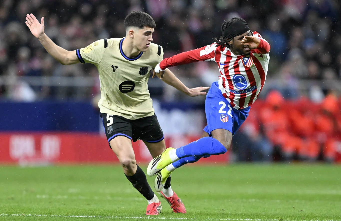 Dwóch piłkarzy rywalizuje o piłkę podczas meczu, zawodnik w kremowym stroju próbuje zatrzymać przeciwnika w czerwono-białych pasach.