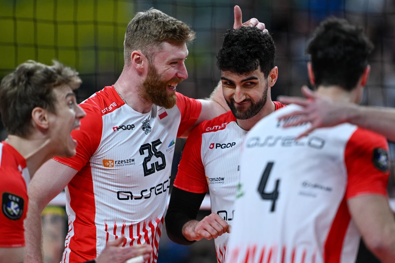 Zawodnicy drużyny siatkarskiej w biało-czerwonych strojach świętują zdobycie punktu, uśmiechając się i przybijając sobie piątki.