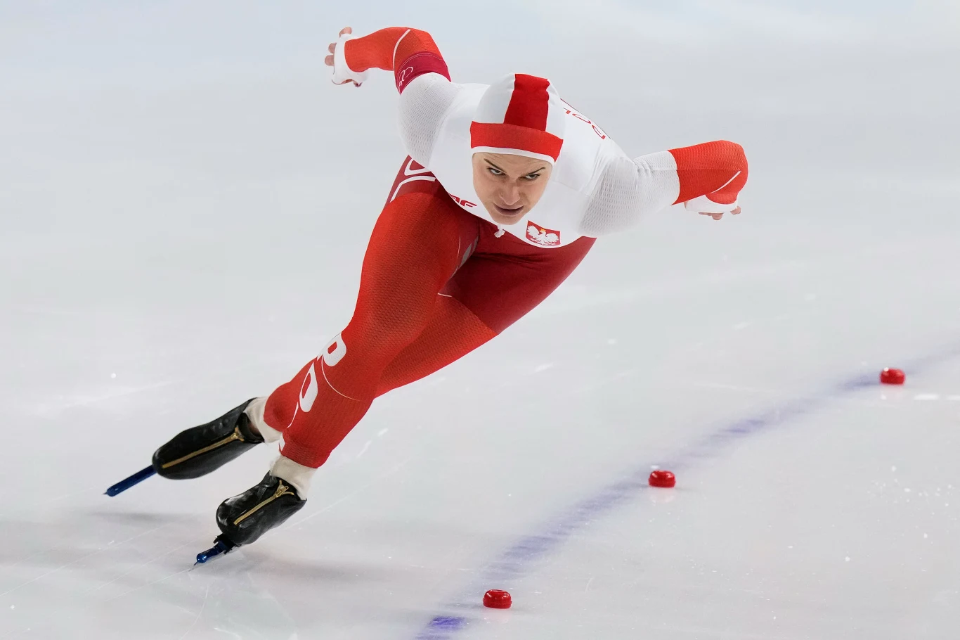 Andżelika Wójcik Łyżwiarz szybki w biało-czerwonym stroju reprezentacji Polski dynamicznie pokonuje zakręt na torze lodowym, koncentrując się na wyścigu.