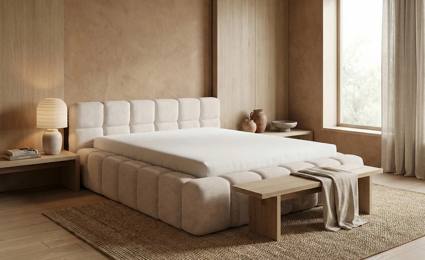 Łóżko chmurka to tapicerowane łóżko z miękkim zagłówkiem o charakterystycznym, zaokrąglonym kształcie Łóżko z tapicerowanym, wyrazistym zagłówkiem ustawione centralnie w jasnej, nowoczesnej sypialni, obok drewniana ławka oraz lampa stołowa na szafce nocnej, minimalistyczny wystrój i naturalne odcienie beżu tworzą spokojną atmosferę.