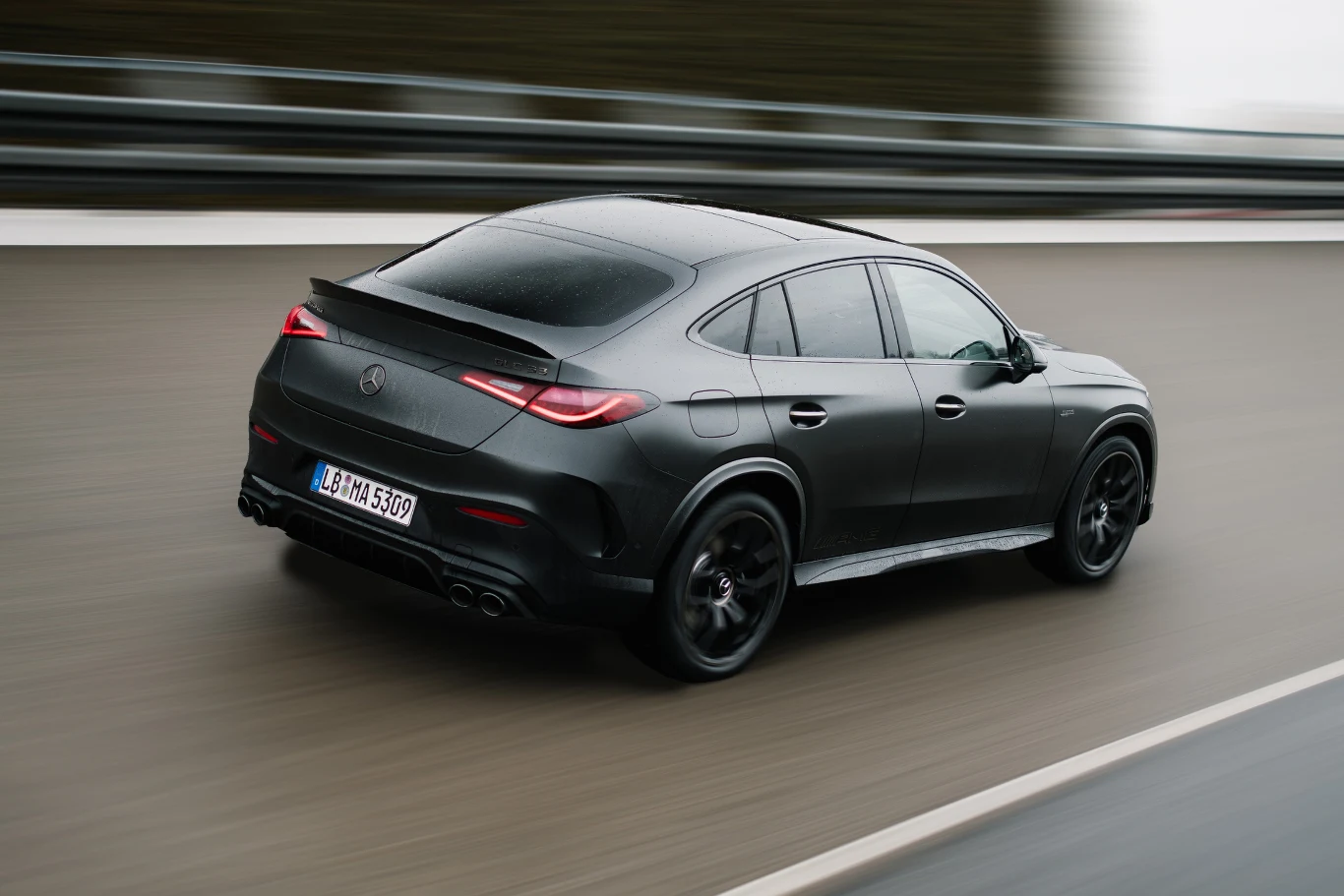 Czarny, sportowy samochód Mercedes SUV coupe poruszający się z dużą prędkością po asfaltowej drodze, widok z tyłu i nieco z góry, smukła sylwetka, zarys barierki oddzielającej pasy ruchu.