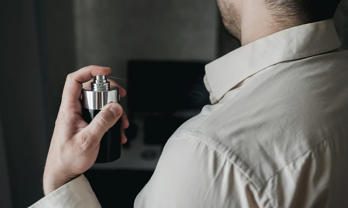 Czy zapach mężczyzny może określać jego usposobienie? Mężczyzna w białej koszuli psika na siebie perfumy, trzymając flakon przy szyi.