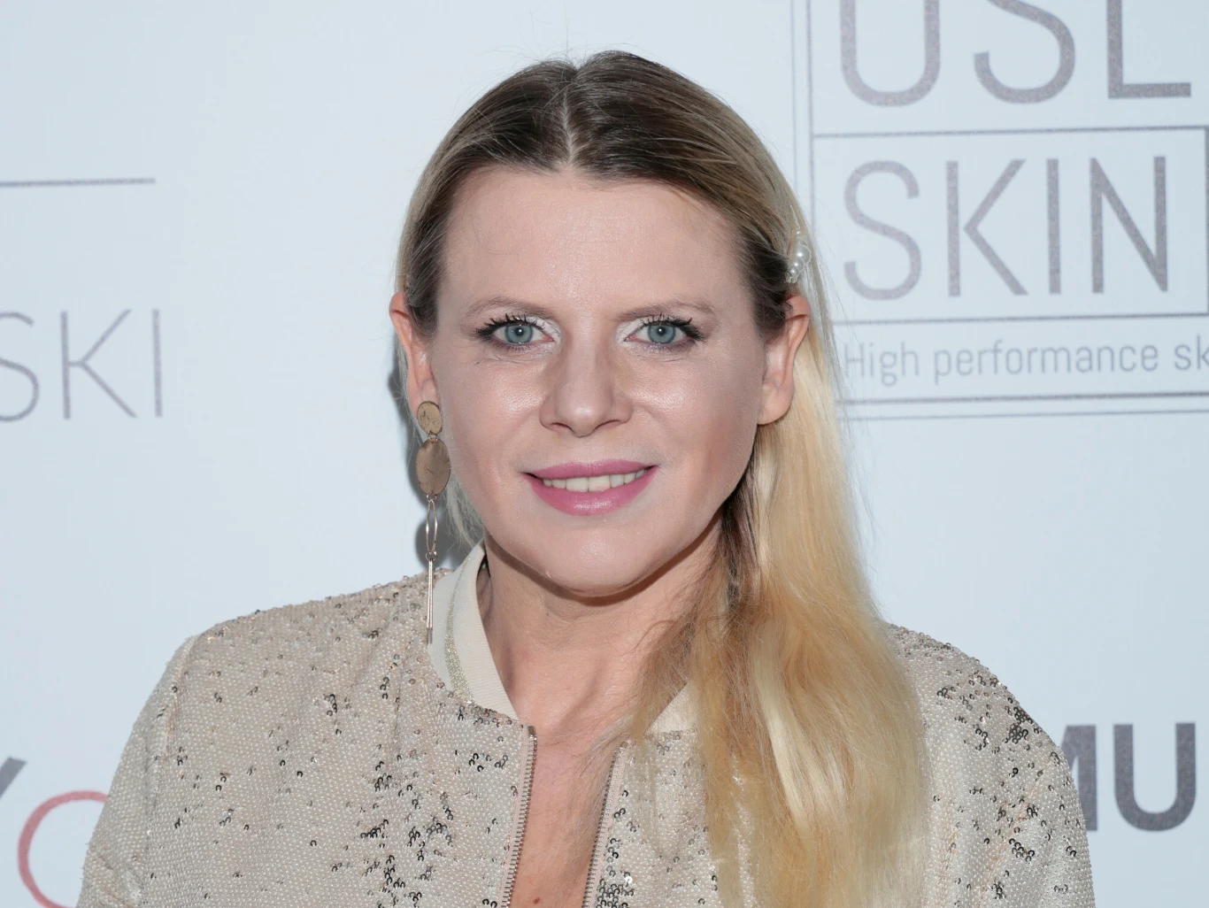 Maria Sadowska wystąpi w nowej edycji "Twoja Twarz Brzmi Znajomo" Kobieta o blond włosach w jasnej, eleganckiej marynarce stoi na tle ściany z logotypami. Uśmiechnięta, z widocznym makijażem, patrzy prosto w obiektyw.