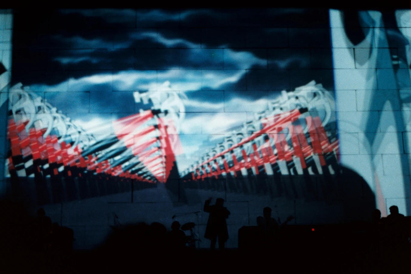 Ilustracja z monumentalnymi, czerwonymi młotami ustawionymi w szeregach pod dramatycznie zachmurzonym niebem, z wyraźnymi odniesieniami do dystopijnej symboliki totalitarnej, na pierwszym planie sylwetki postaci w cieniu.