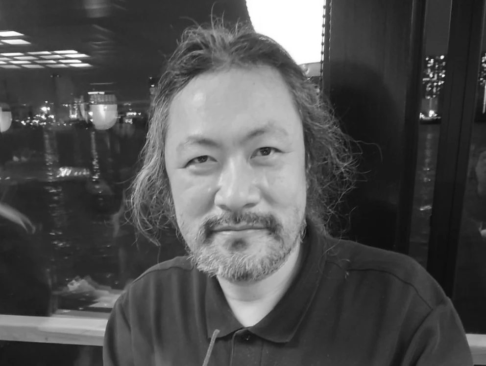 Shutao Iida zmarł po ciężkiej chorobie. Jeden z ojców Castlevanii to legenda sektora gier Mężczyzna z dłuższymi, siwymi włosami i brodą, ubrany w ciemną koszulę, siedzi w pomieszczeniu z ciemnym tłem oraz odbiciem świateł w oknie za nim