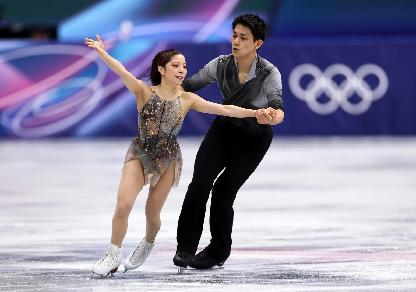 Riku Miura i Ryuichi Kiha Pary łyżwiarzy figurowych wykonujący wspólny układ na lodowisku podczas zawodów olimpijskich, w tle widoczne logo igrzysk olimpijskich.