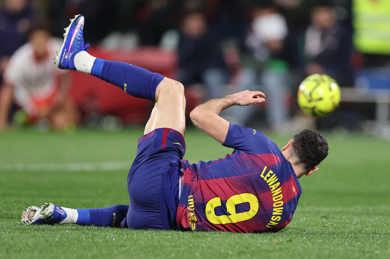 Robert Lewandowski na obiekcie Girony Piłkarz w barwach FC Barcelony upada na murawę podczas meczu, z piłką toczącą się obok niego, dynamiczna sportowa scena uchwycona w trakcie rywalizacji.