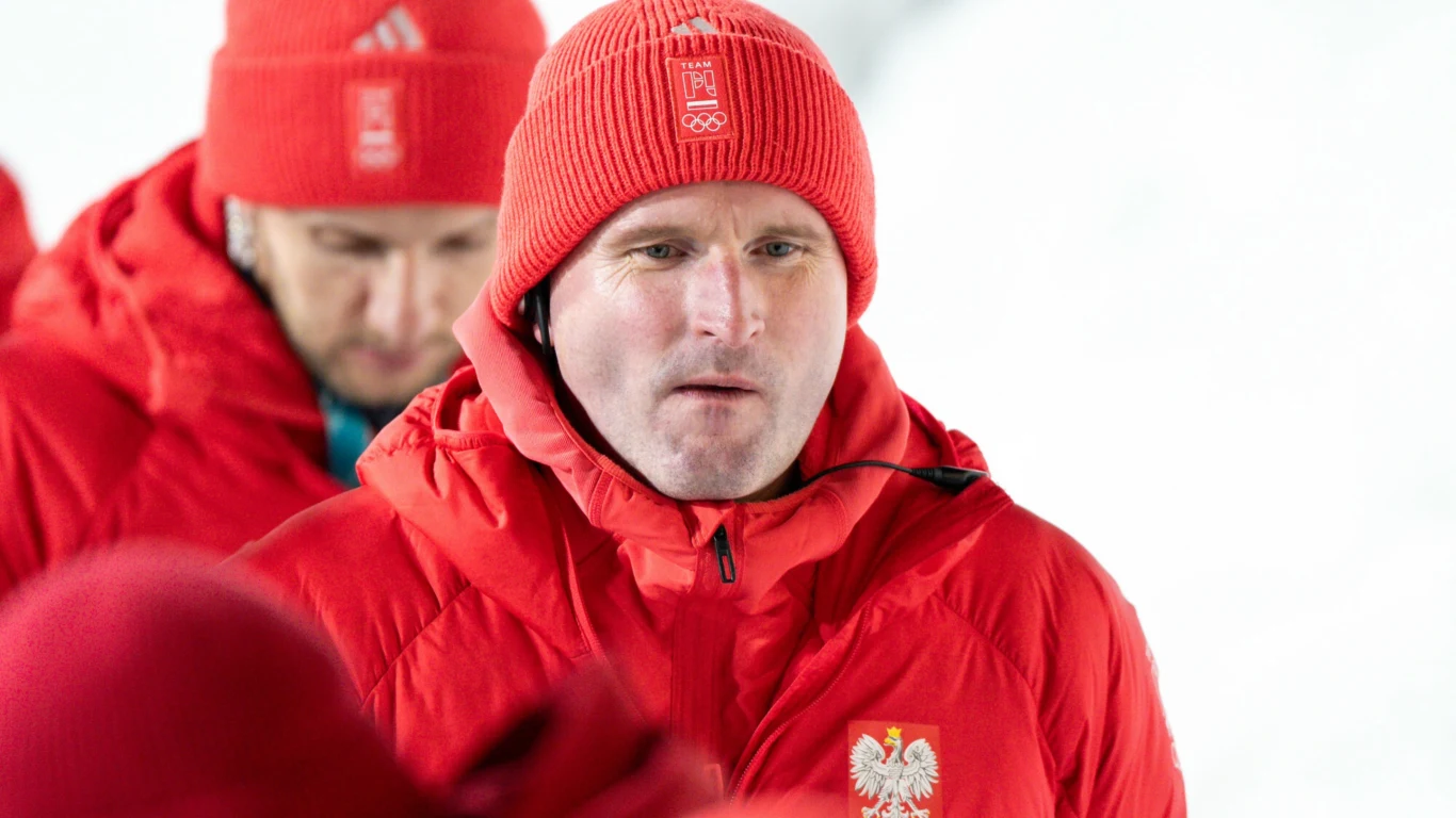 Maciej Maciusiak Mężczyzna ubrany w czerwoną zimową kurtkę i czerwoną czapkę z logotypem reprezentacji Polski, na kurtce widoczne godło Polski, w tle inne osoby w podobnych strojach.