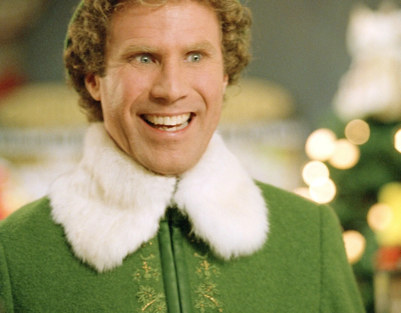 Will Ferrell w filmie "Elf" Mężczyzna w zielonym kubraku z białym futrzanym kołnierzem, uśmiechnięty, w tle rozmyte światełka i świąteczna dekoracja.