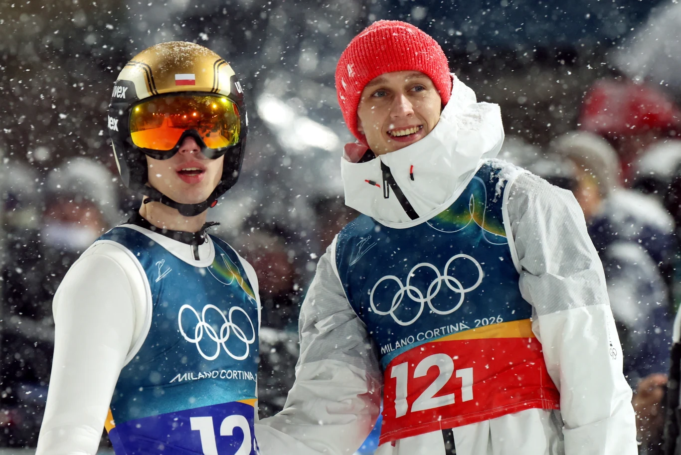 Kacper Tomasiak i Paweł Wąsek Dwóch sportowców w zimowych strojach z numerami startowymi podczas igrzysk olimpijskich w otoczeniu padającego śniegu, jeden z zawodników ma na głowie kask i gogle, drugi czerwoną czapkę.