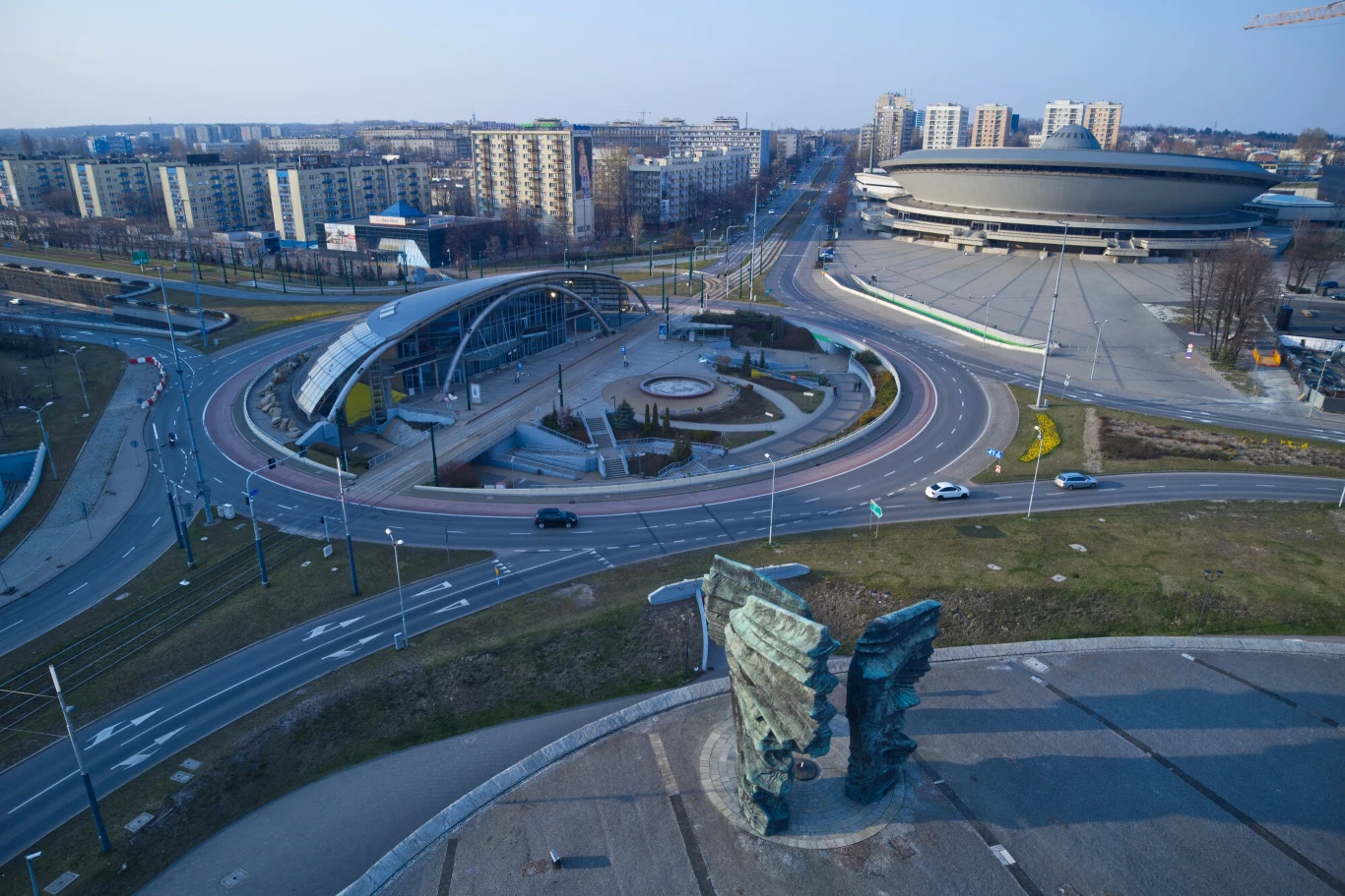 Centrum Katowic Panorama miasta z widokiem na charakterystyczny okrągły budynek Spodka, monumentalny Pomnik Powstańców Śląskich na pierwszym planie, nowoczesny węzeł komunikacyjny oraz otaczające wieżowce mieszkalne.
