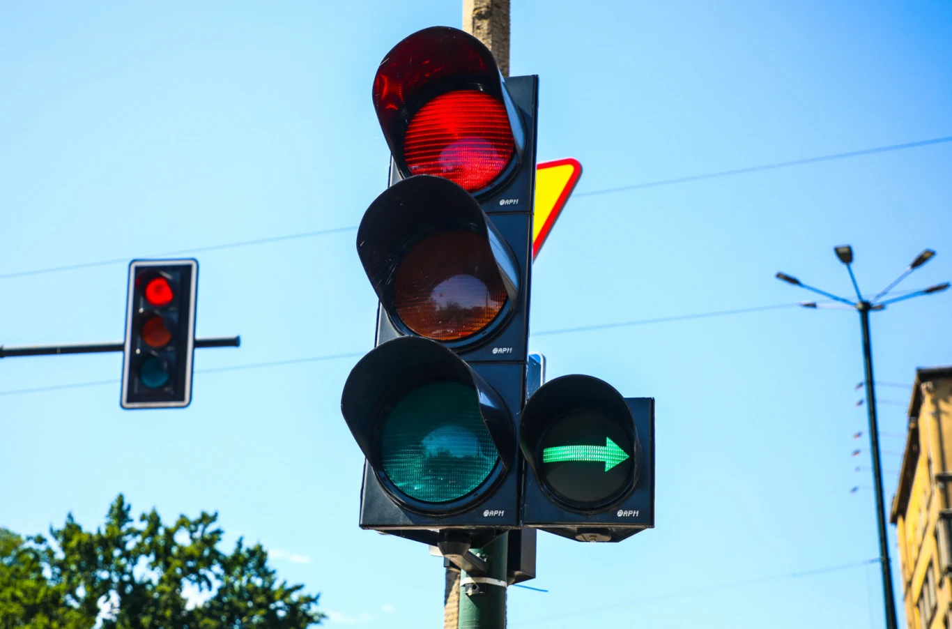 Skręcając na skrzyżowaniu kierowca pojazdu ma obowiązek ustąpić pierwszeństwa pieszemu. Sygnalizacja świetlna z czerwoną lampą oraz zieloną strzałką w prawo na tle nieba i fragmentów ulicznych latarni.