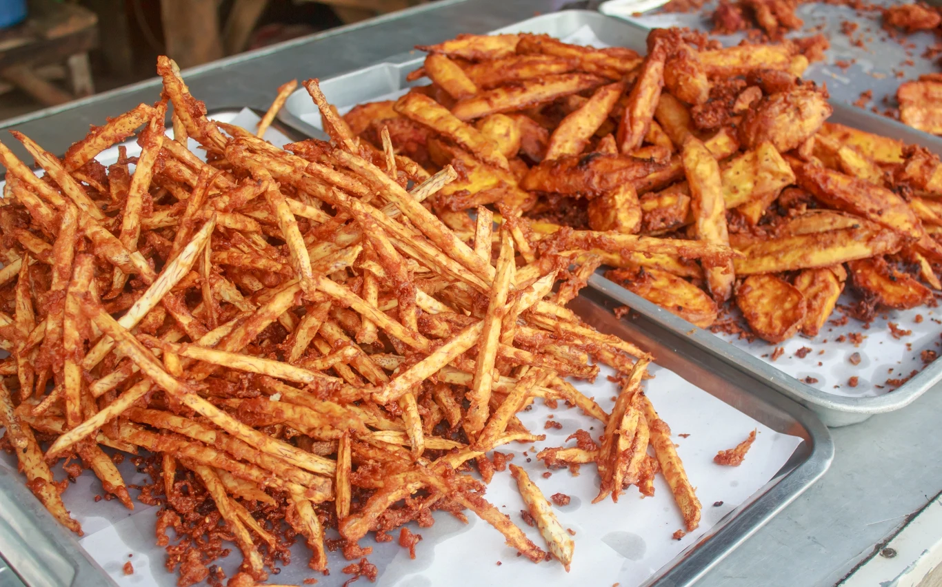 Dwie blachy wypełnione smażonymi batatami, jedna z cienkimi frytkami, druga z grubszymi kawałkami. Wszystko wygląda na świeżo usmażone i chrupiące, podane na papierze do pieczenia.