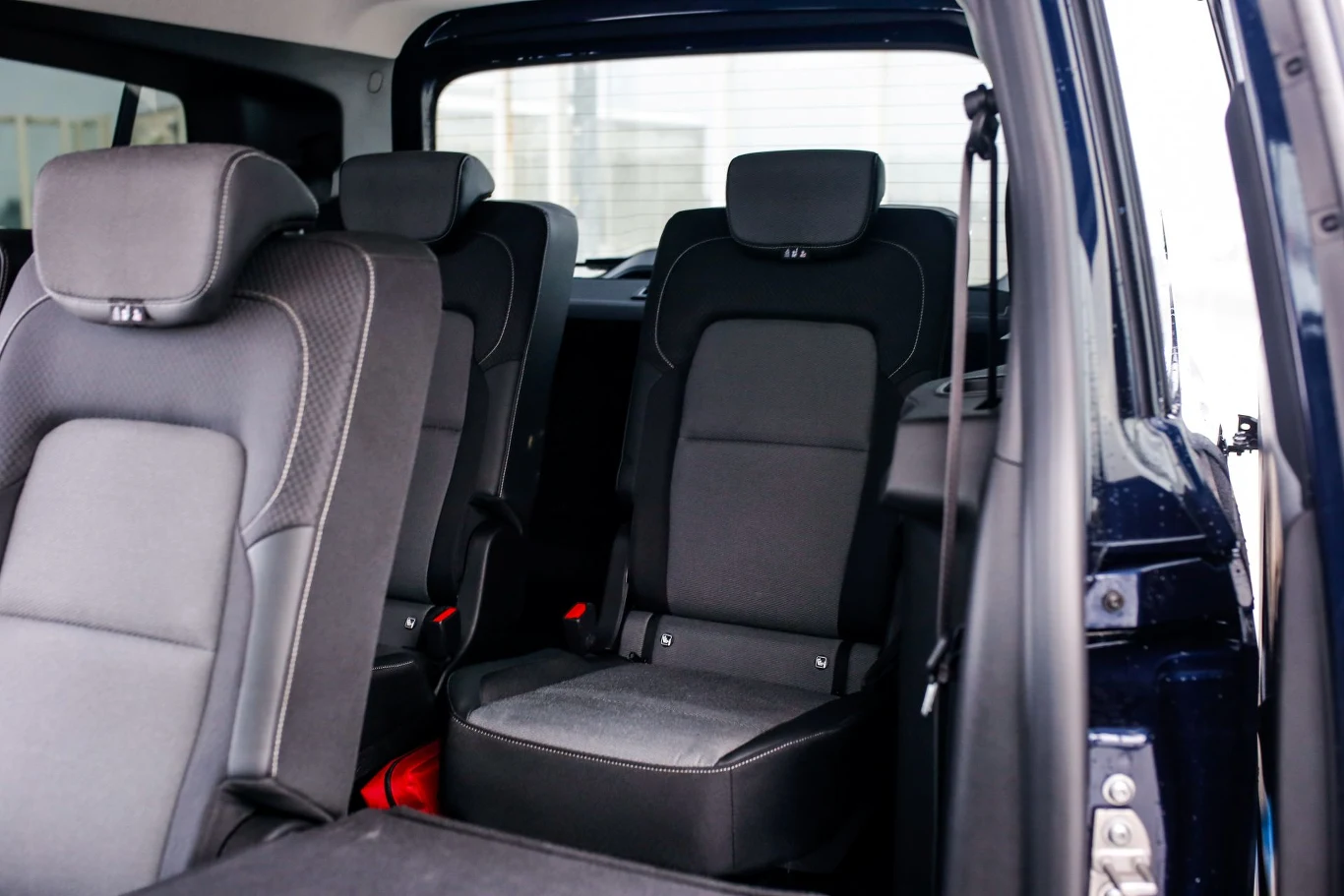 W trzecim rzędzie foteli spokojnie zasiądą nie tylko dzieci. Wnętrze samochodu z trzema siedzeniami w drugim rzędzie, tapicerka w odcieniach czerni i szarości, widoczne pasy bezpieczeństwa, otwarte drzwi po prawej stronie umożliwiające wejście.
