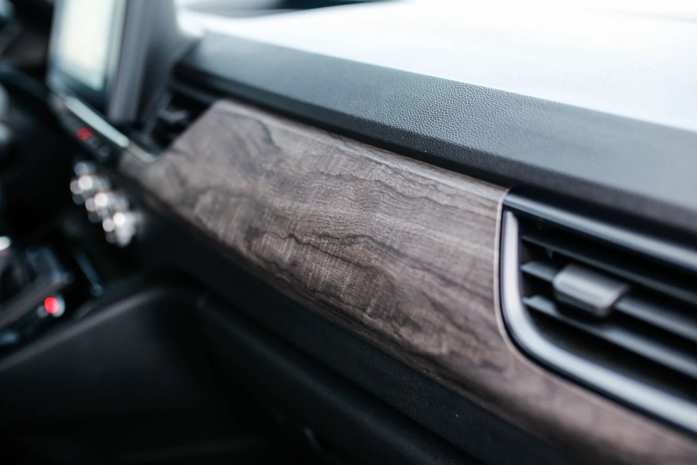 Imitujący drewno dekor na desce rozdzielczej jest jedyną irytującą rzeczą wewnątrz tego auta. Deska rozdzielcza samochodu z elementami wykończenia przypominającymi drewno oraz widocznymi nawiewami powietrza i fragmentami konsoli środkowej.