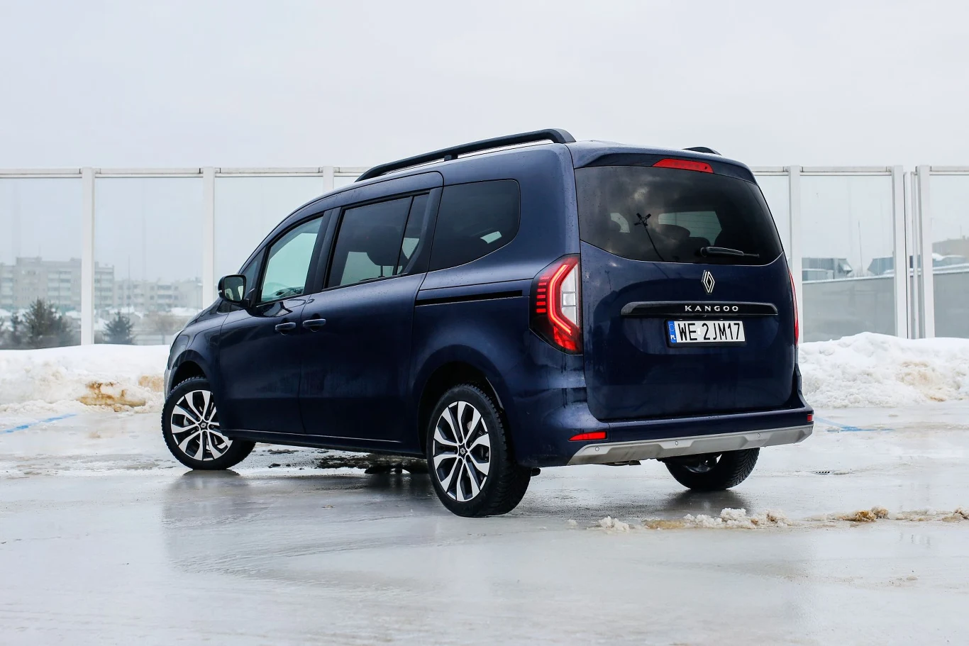 Renault Grand Kangoo ma 4 911 mm długości. Granatowy minivan Renault Kangoo zaparkowany na ośnieżonym i oblodzonym parkingu, widoczne są zabudowania w tle oraz numer rejestracyjny pojazdu.
