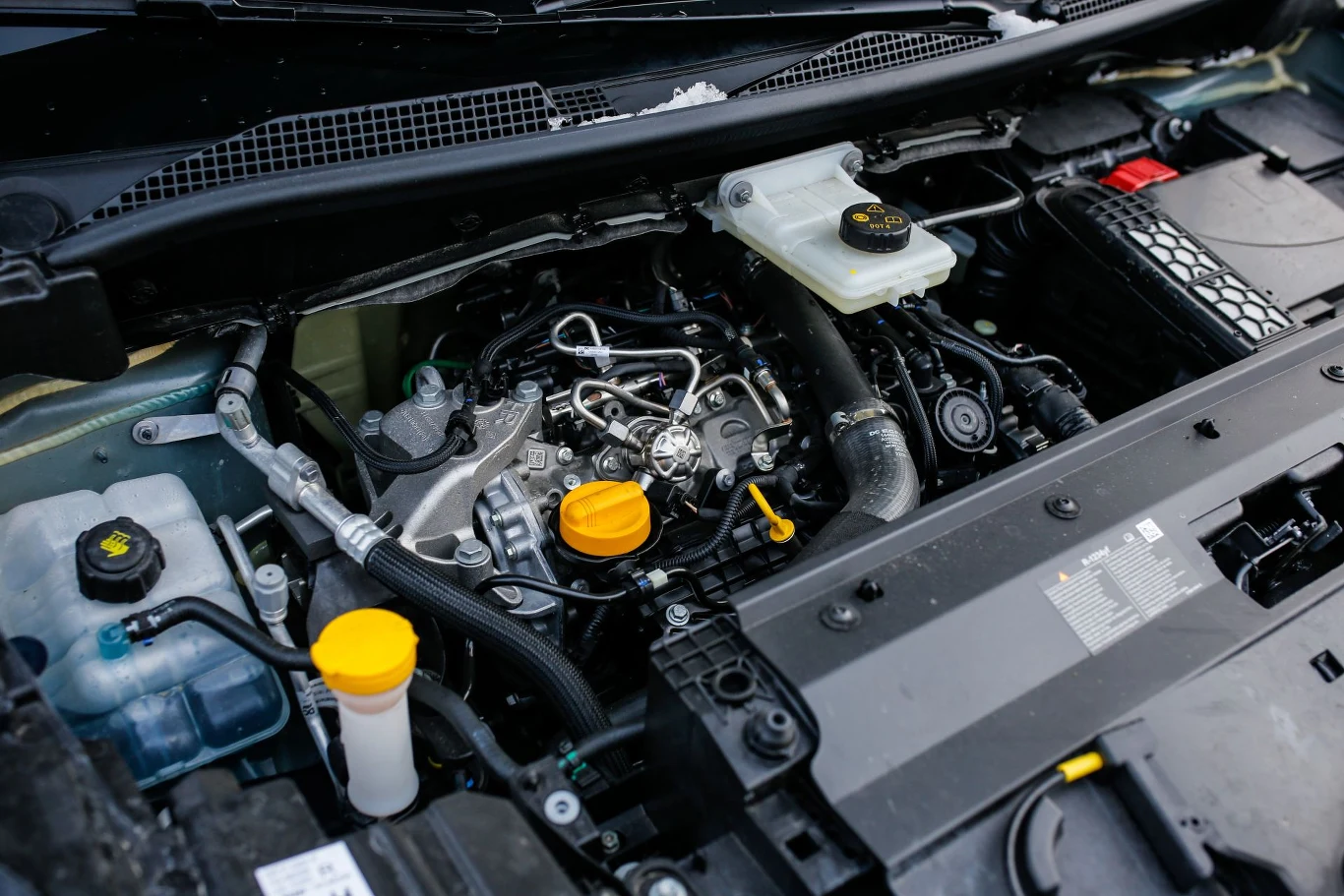 Renault Grand Kangoo wyposażone może być w silnik benzynowy o pojemności 1,4 l (130 KM) lub 1,5-litrową jednostkę wysokoprężną (115 KM). Silnik samochodowy z widocznymi przewodami, zbiornikiem płynu hamulcowego, korkami do napełniania oleju i płynów eksploatacyjnych, elementami metalowymi i plastikowymi w komorze silnika.