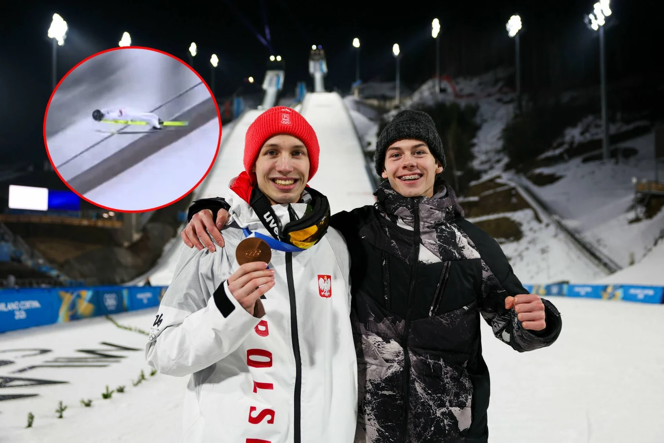 Dwóch młodych mężczyzn na tle rozświetlonej skoczni narciarskiej pozuje do zdjęcia, jeden z nich trzyma medal, obaj są uśmiechnięci. W lewym górnym rogu widoczny jest mały podgląd narciarskiego skoku.