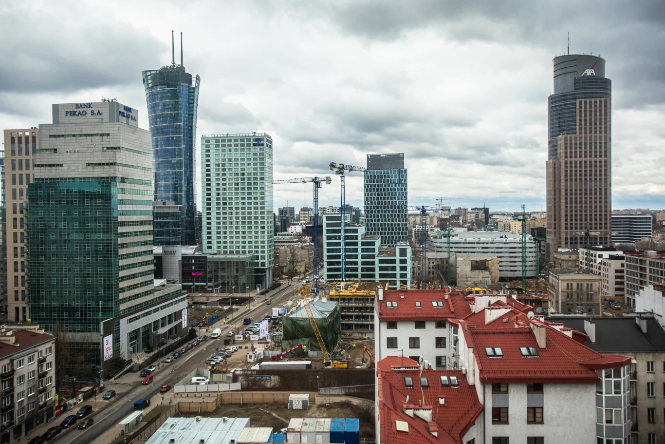 Pekao Tower przejdzie do historii. W centrum Warszay powstanie nowy budynek Panorama nowoczesnego centrum miasta z dominującymi wysokimi biurowcami, żurawiami budowlanymi oraz zabudową mieszkalną w pierwszym planie, pod zachmurzonym niebem.