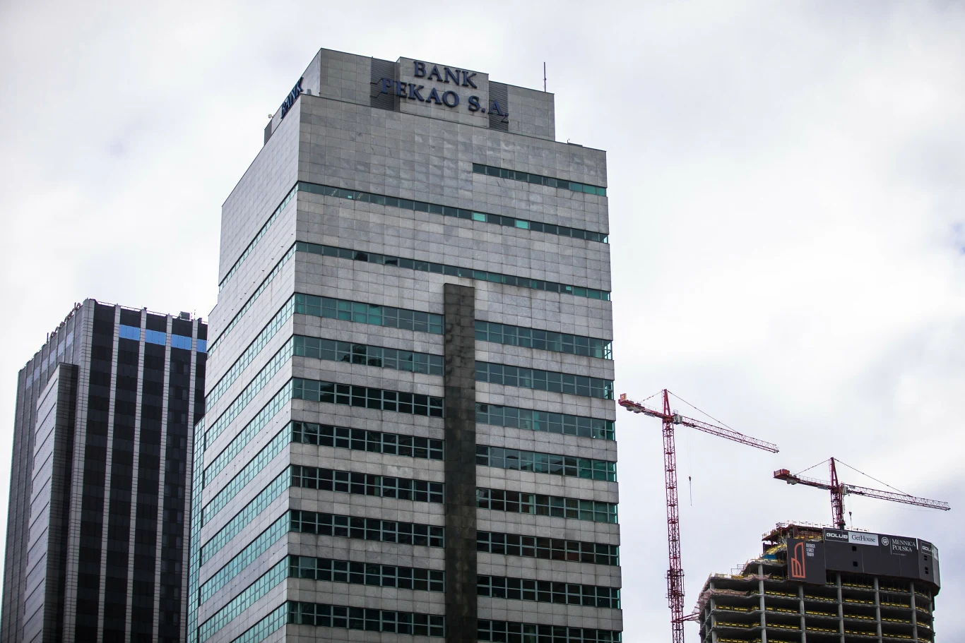 Pekao Tower przejdzie do historii. W centrum Warszay powstanie nowy budynek Wysoki budynek z napisem Bank Pekao S.A. na dachu, otoczony innymi wieżowcami oraz żurawiami budowlanymi na tle pochmurnego nieba.