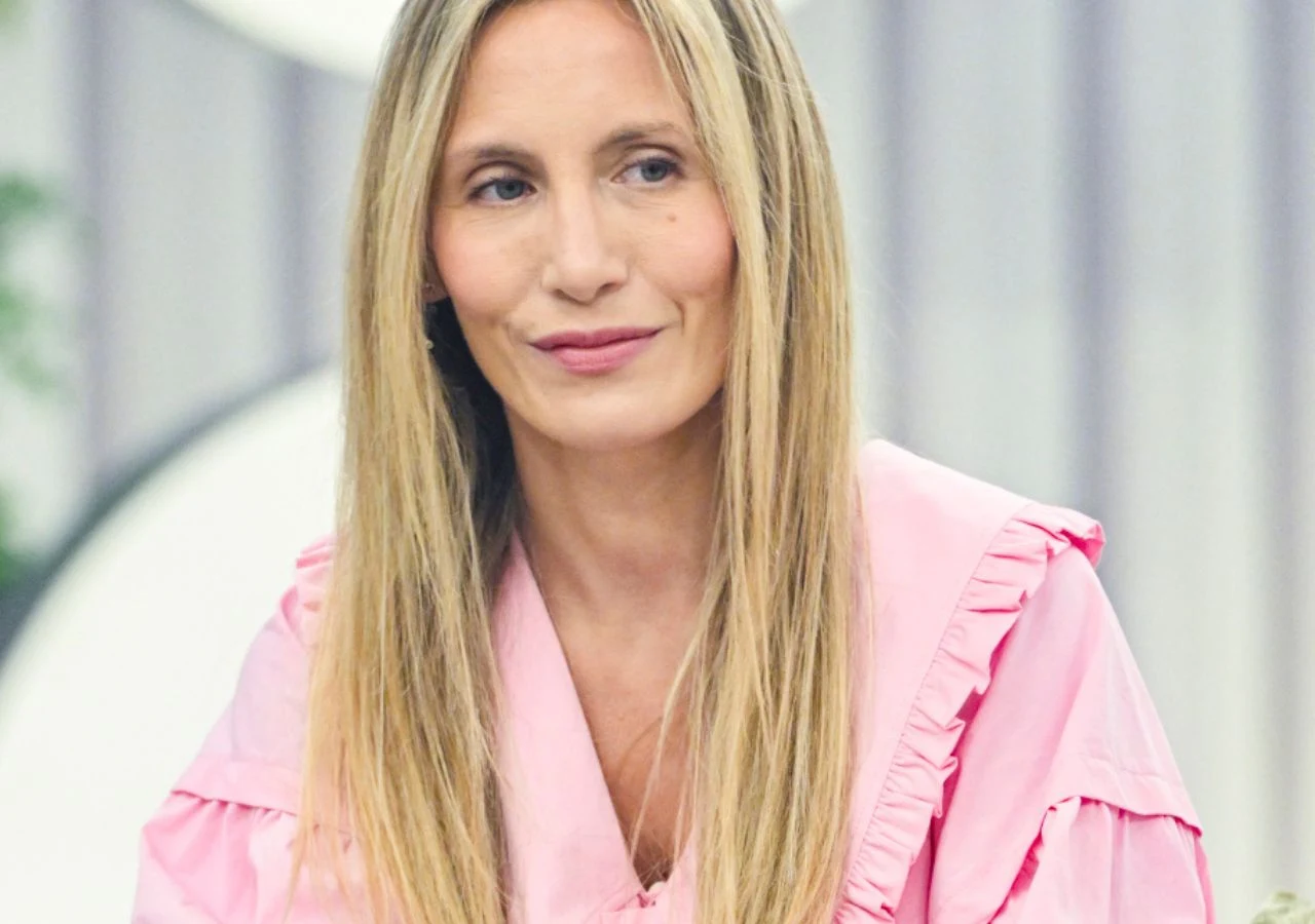 Pola Wiśniewska Kobieta o długich blond włosach, ubrana w różową bluzkę z falbanami, siedzi w jasnym pomieszczeniu. W tle widoczne rozmyte elementy dekoracyjne.