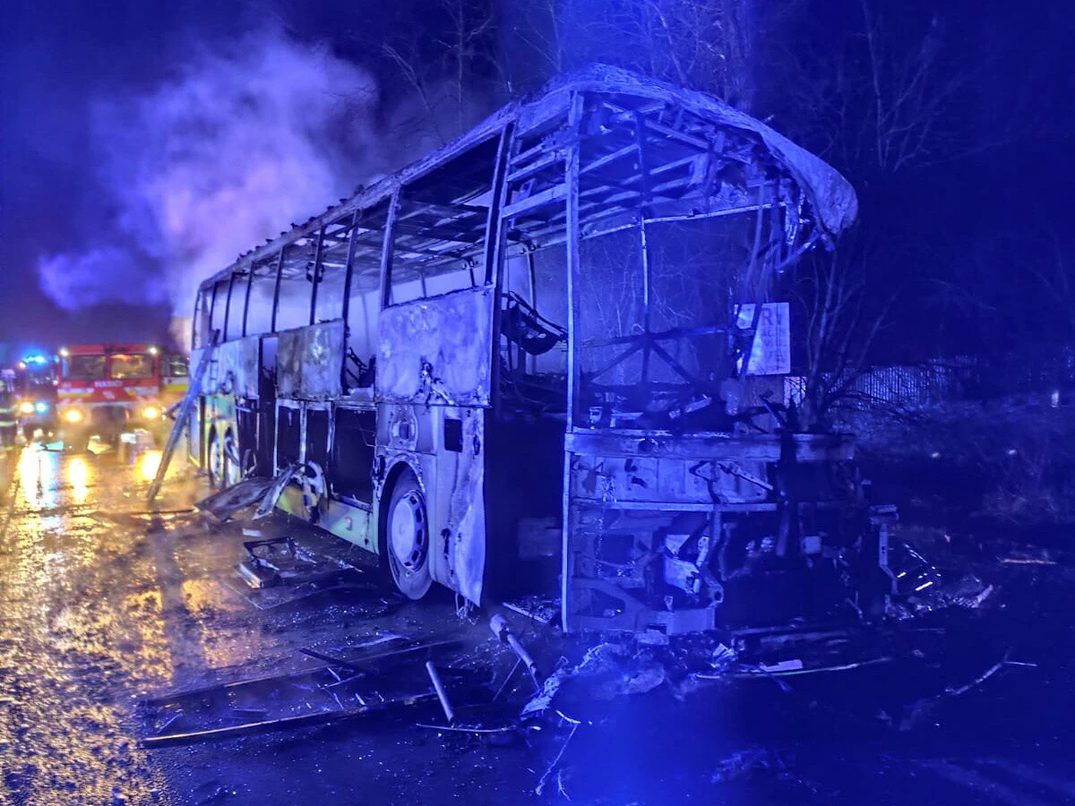 Polski autokar zderzył się z ciężarówką na Słowacji Wrak spalonego autobusu stojący na mokrej nawierzchni, dookoła unoszący się dym i widoczne światła pojazdów straży pożarnej w tle.